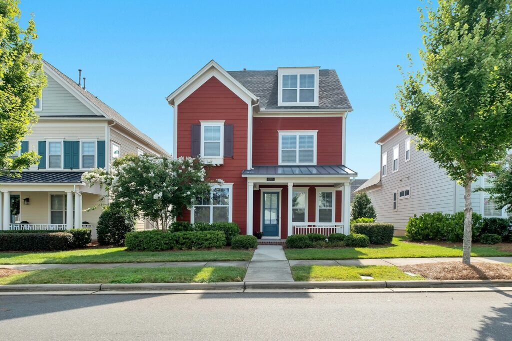 Red two story California real estate house with porch and green bushes
