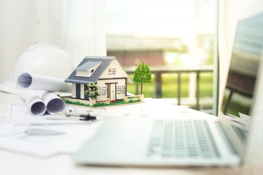 Model house on desk with blueprints laptop and hard hat