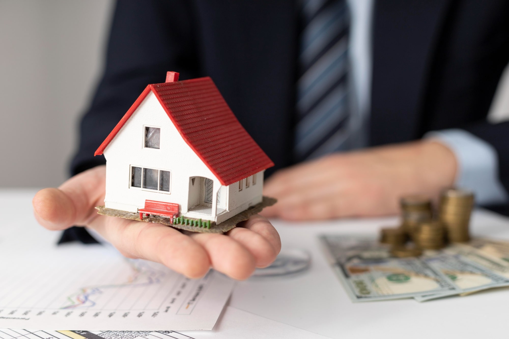 Person holding model house with coins and money on documents