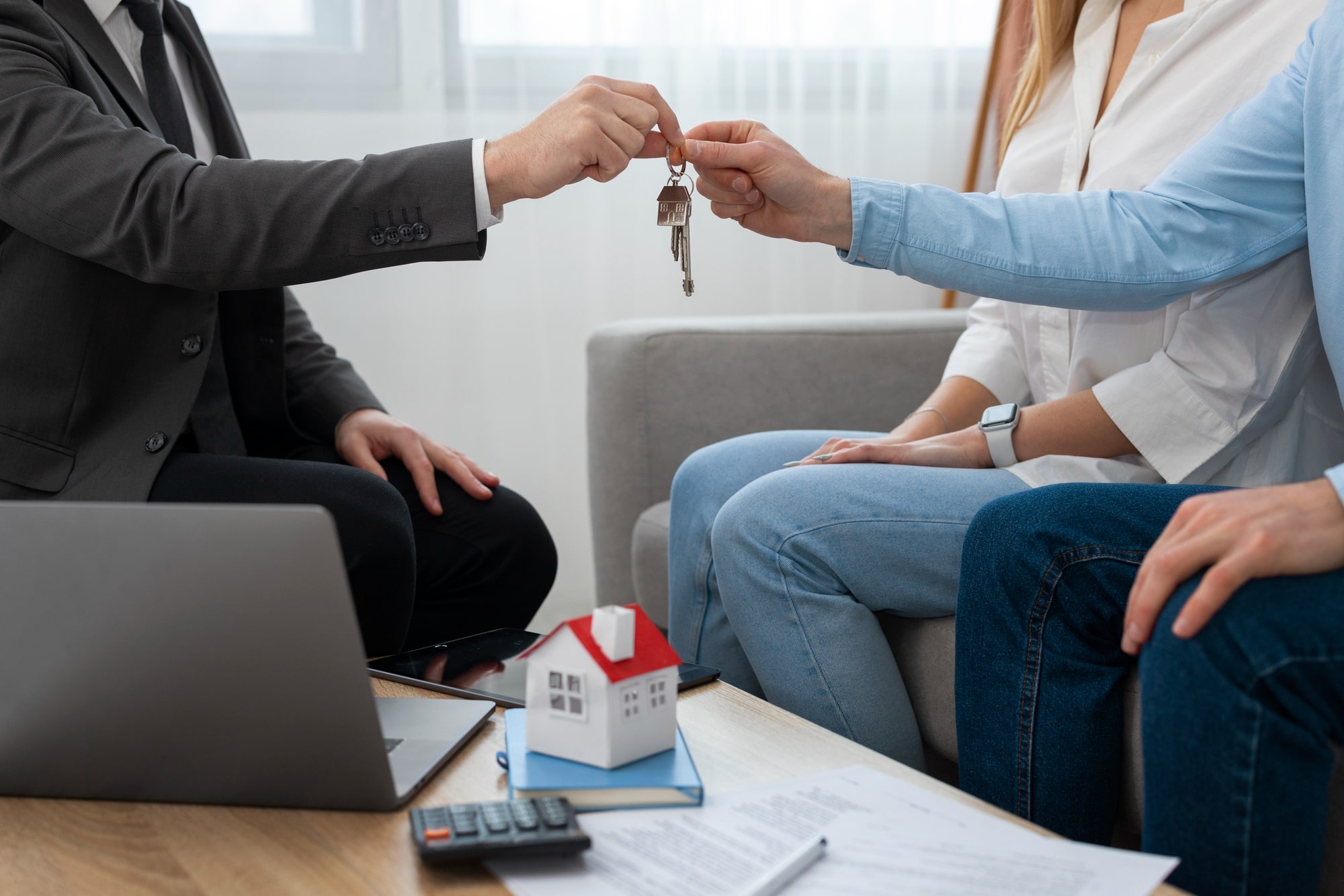 Person giving house keys with model house and papers on table