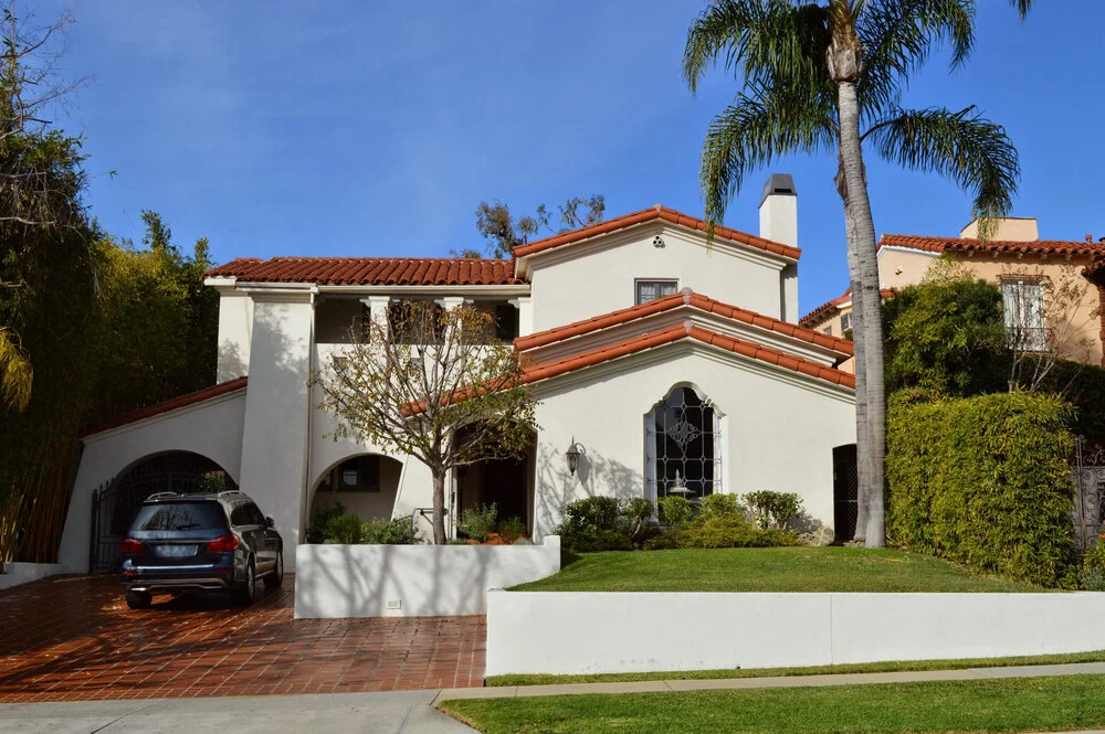 Two story California real estate house with white exterior red tile roof driveway and palm trees
