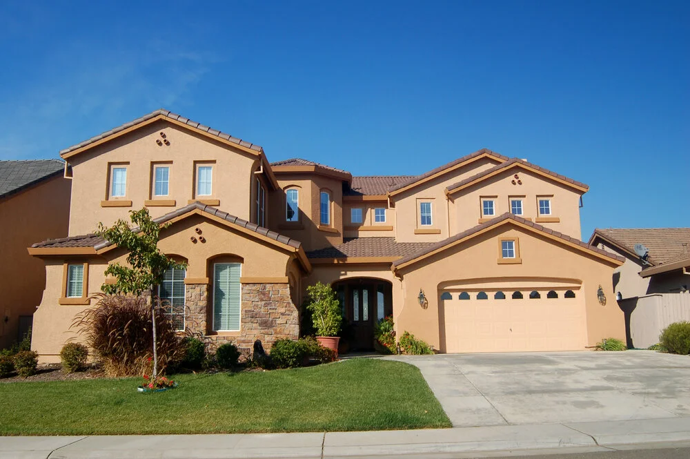 Luxury two story California real estate house with beige exterior stone accents driveway and trees