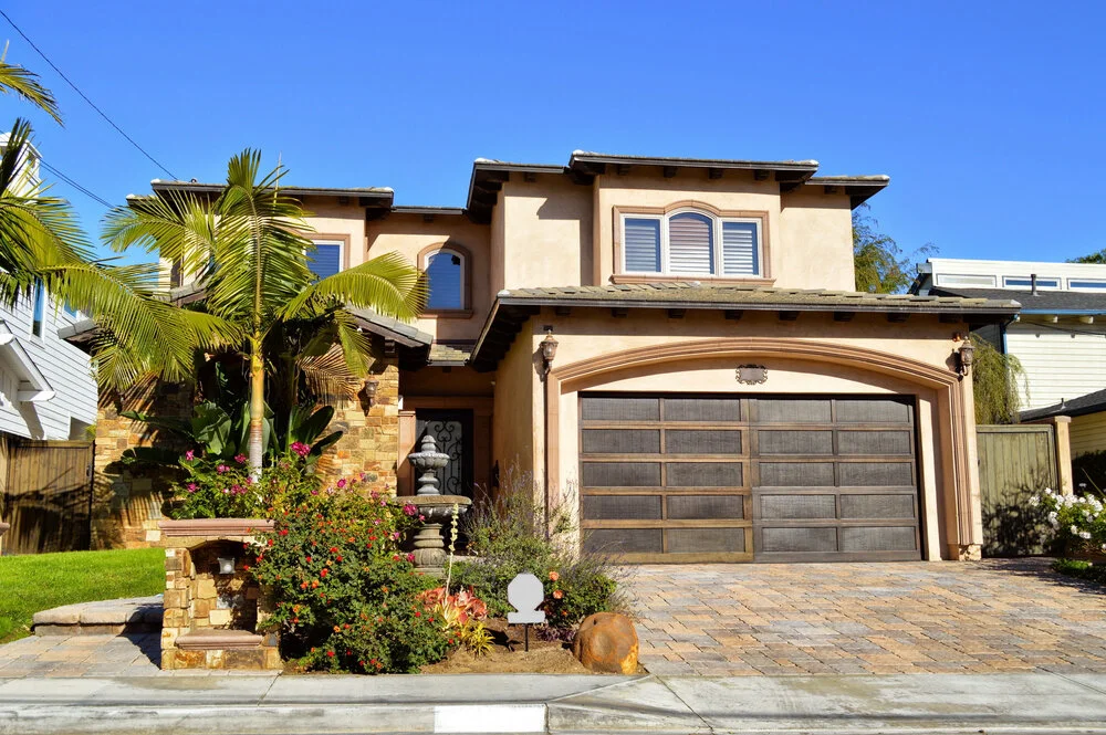 Two story California real estate house with brown exterior palm trees stone pathway and garage