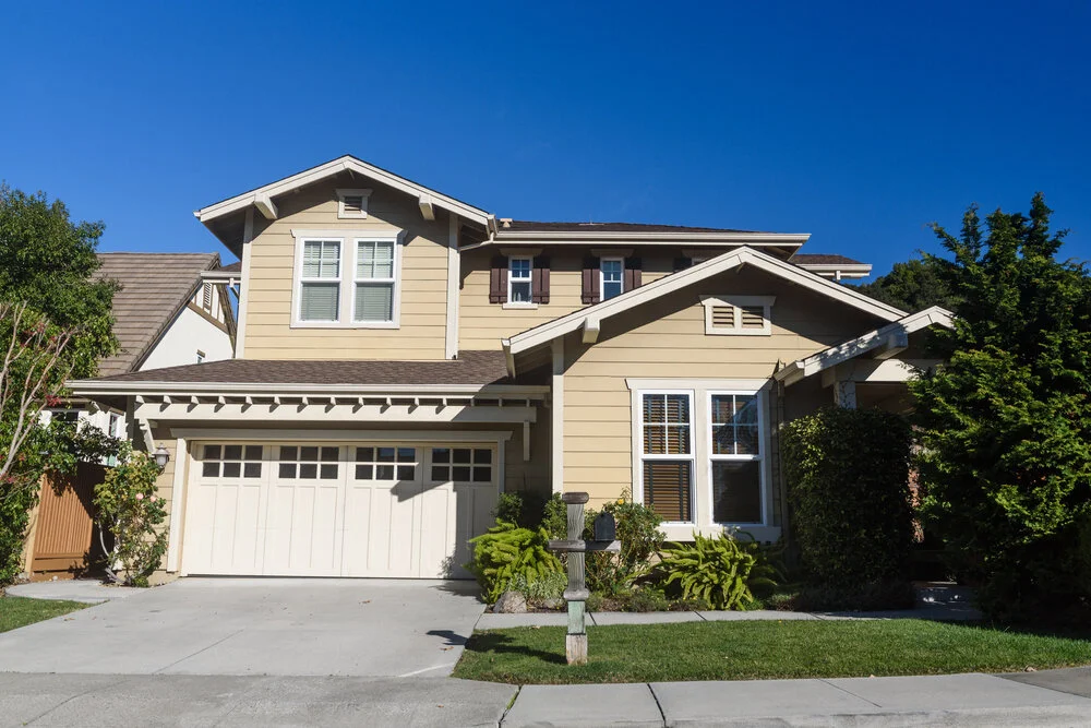 Two story California real estate house with beige siding garage and green shrubs